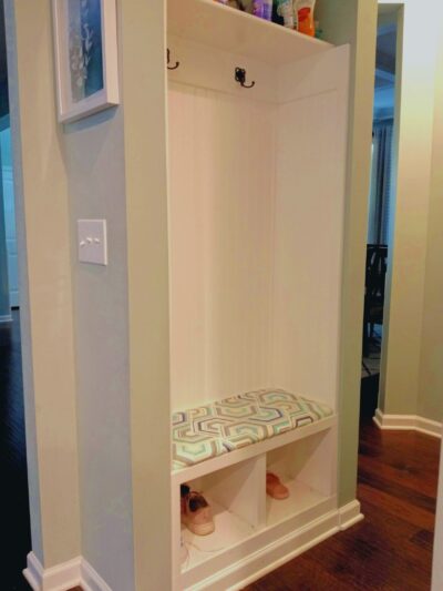A small alcove is lined with beadboard and has a built-in bench with coat hooks and a shelf above.